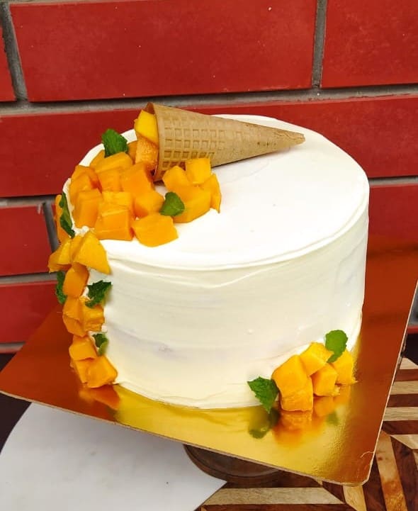 White mango cake topped with fresh mango cubes, mint and a waffle cone