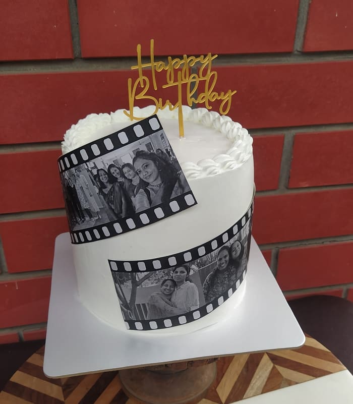 White birthday cake decorated with photo film strips and a Happy Birthday topper